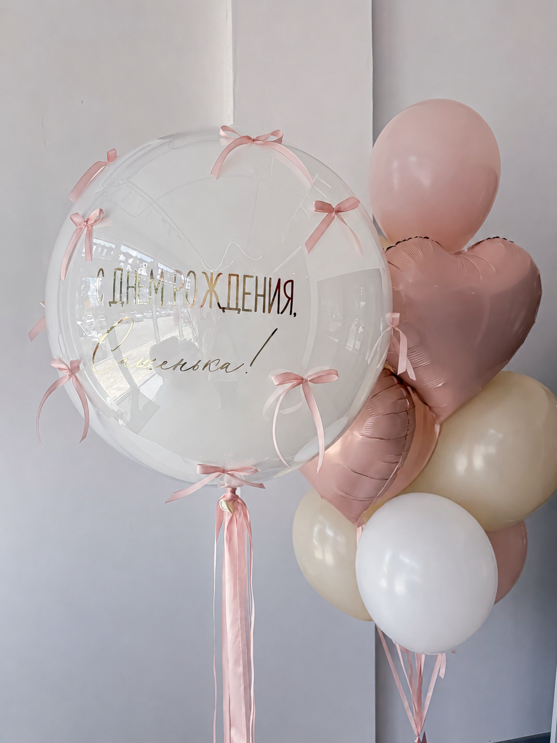 Композиция для девочки с большим прозрачным Bubble с поздравительной надписью и розовыми бантиками, фольгированными сердцами и нежно-розовыми воздушными шарами